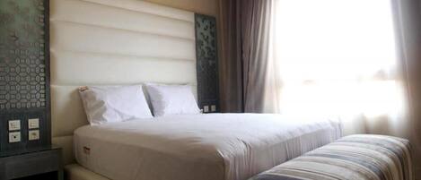 A hotel room with a large bed, a bedside table, and a window with curtains.