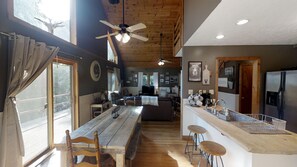 A cozy cabin interior with a wooden dining table, bar stools, a ceiling fan, and a kitchen area with a refrigerator. - Unwind & Refresh at Memories Made Cabin (Tecumseh)