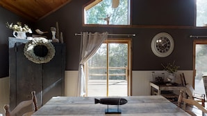 Een rustiek houten interieur met een eettafel, een decoratieve krans, een vogelbeeldje en een klok aan de muur.