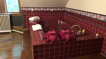 A bathroom with a red-tiled bathtub, a wooden radiator, and a window with floral curtains.