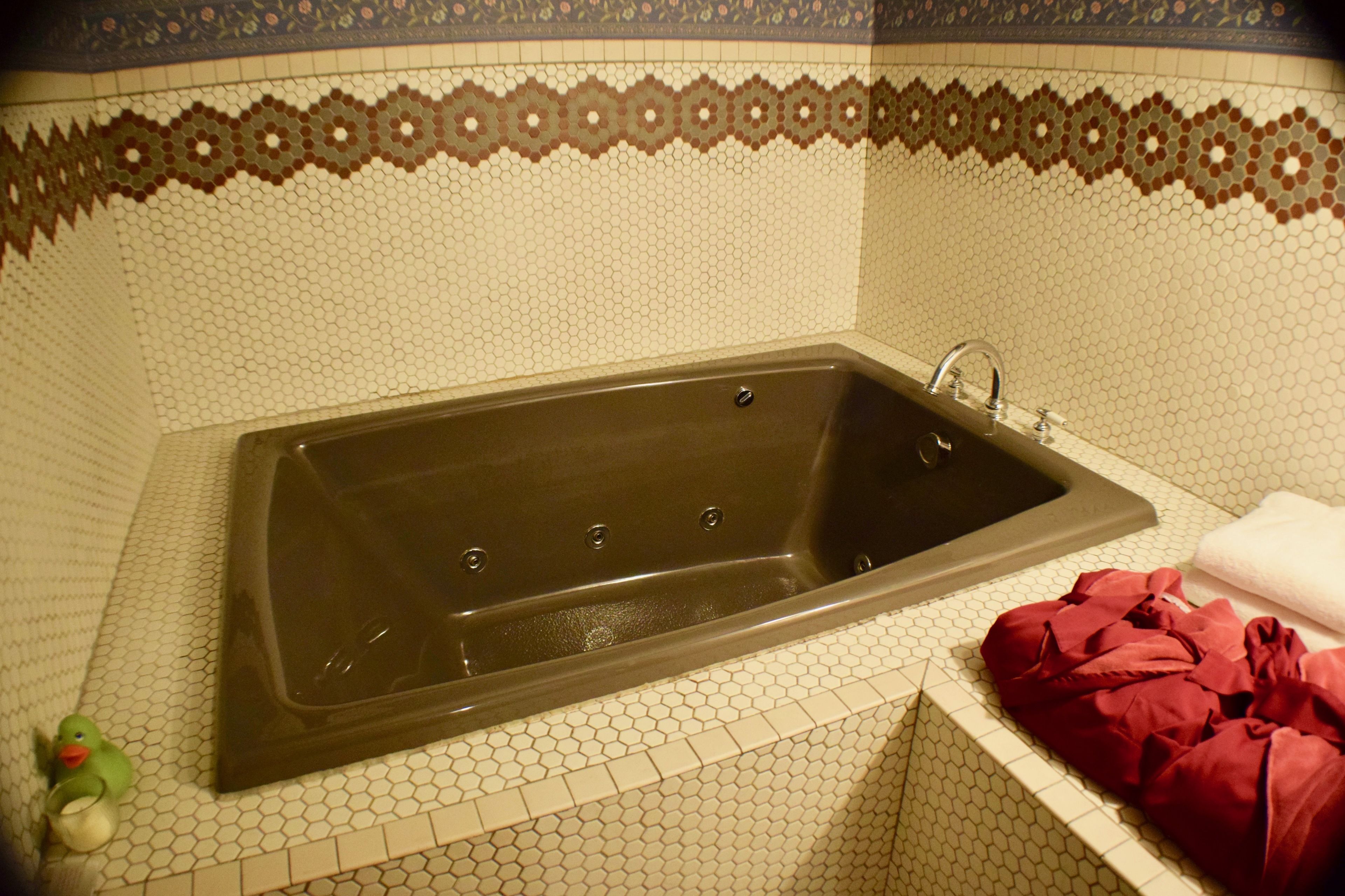 Ein Badezimmer mit einer großen Badewanne, einem Waschbecken und einem Fliesenboden mit dekorativer Bordüre.
