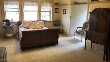 A bedroom with a large bed, two chairs, a dresser, and a desk with a lamp.