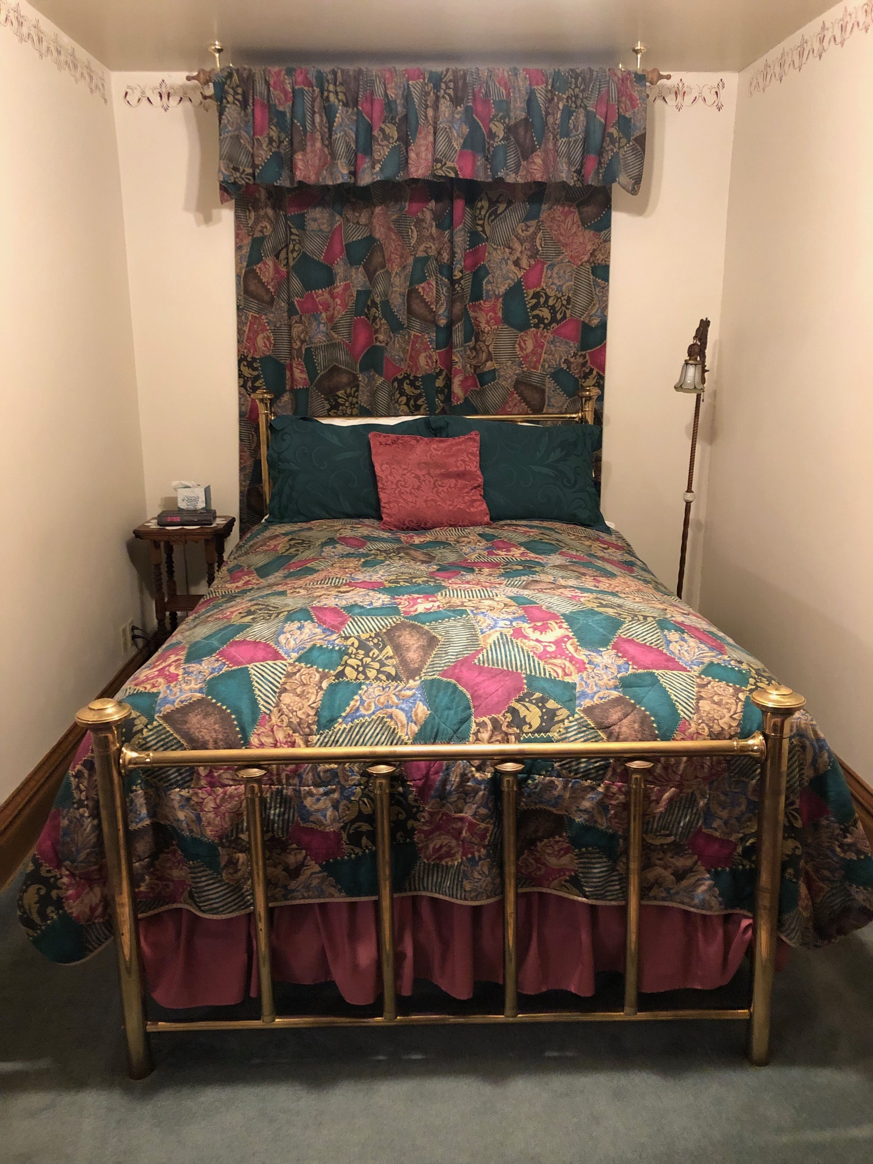 A bed with a patterned quilt, a red pillow, and a gold frame.