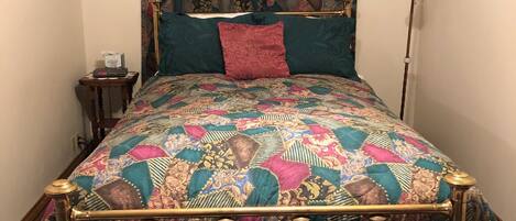 A bed with a patterned quilt, a red pillow, and a gold frame.