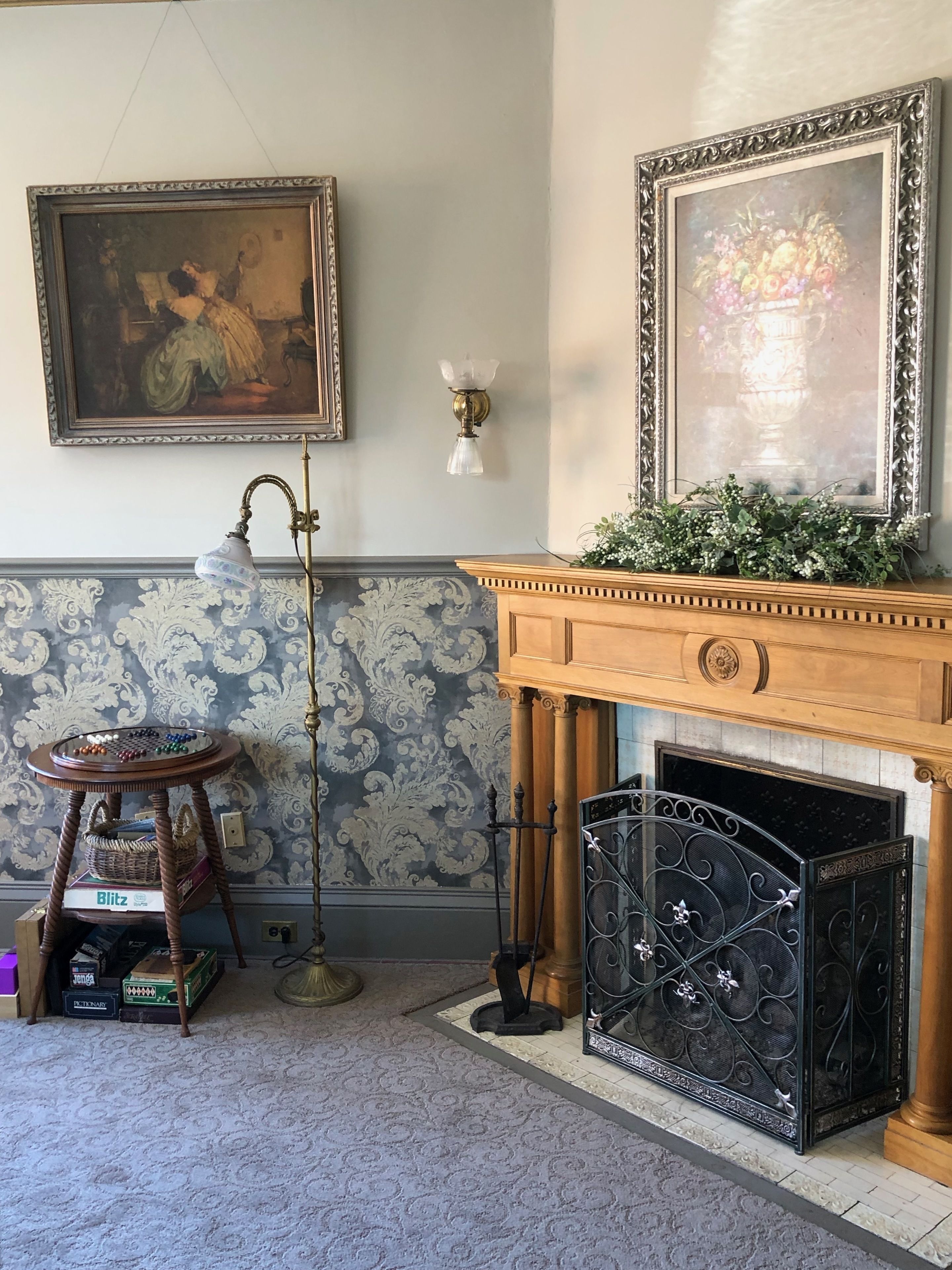 A room with a fireplace, a chandelier, a table with a board game, and two framed paintings on the wall.