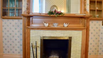 A fireplace with a wooden mantel, a mirror above it, and a floral wallpaper pattern on the walls.