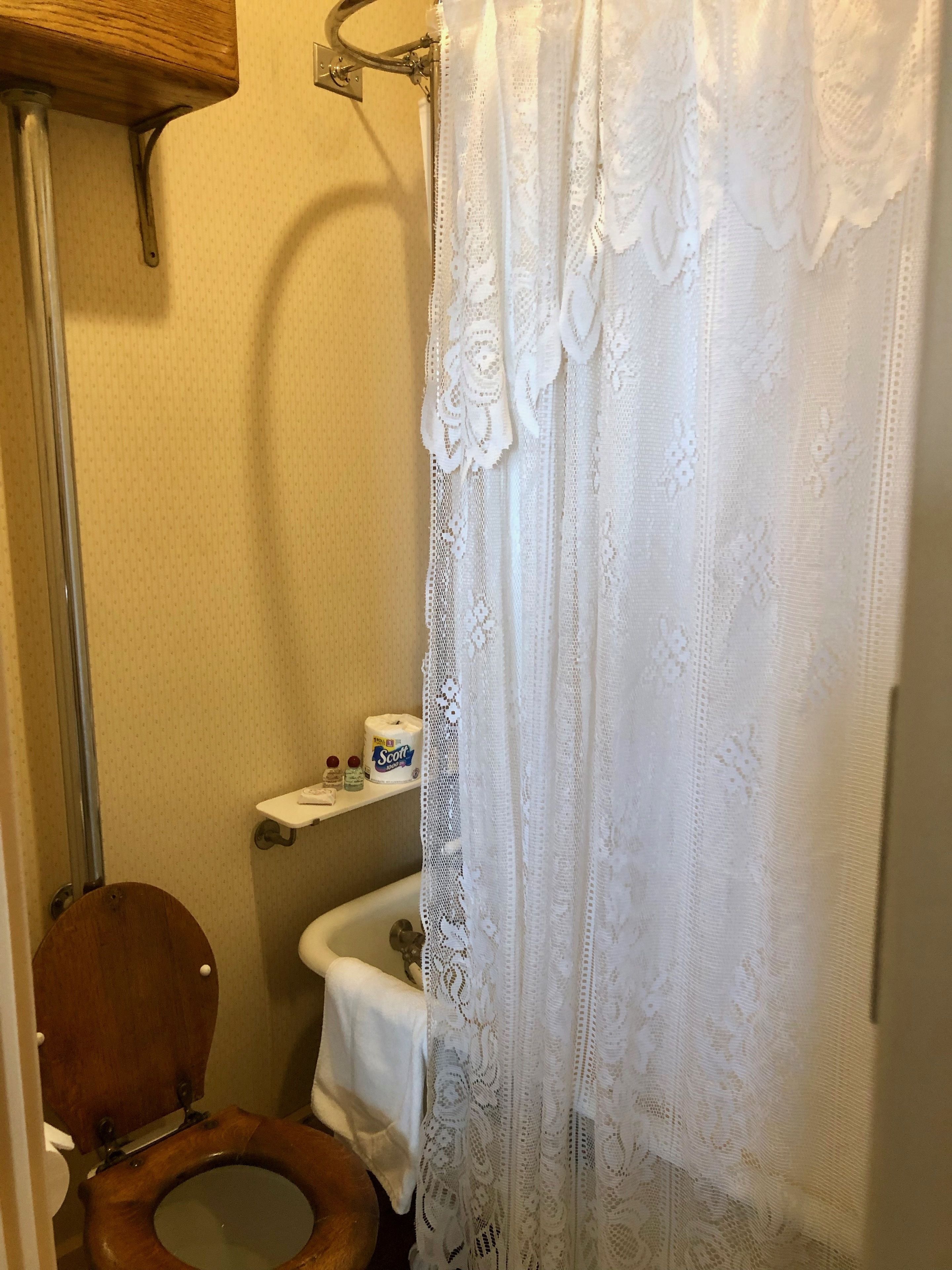 Een badkamer met een houten toilet, een witte wastafel en een douchegordijn.
