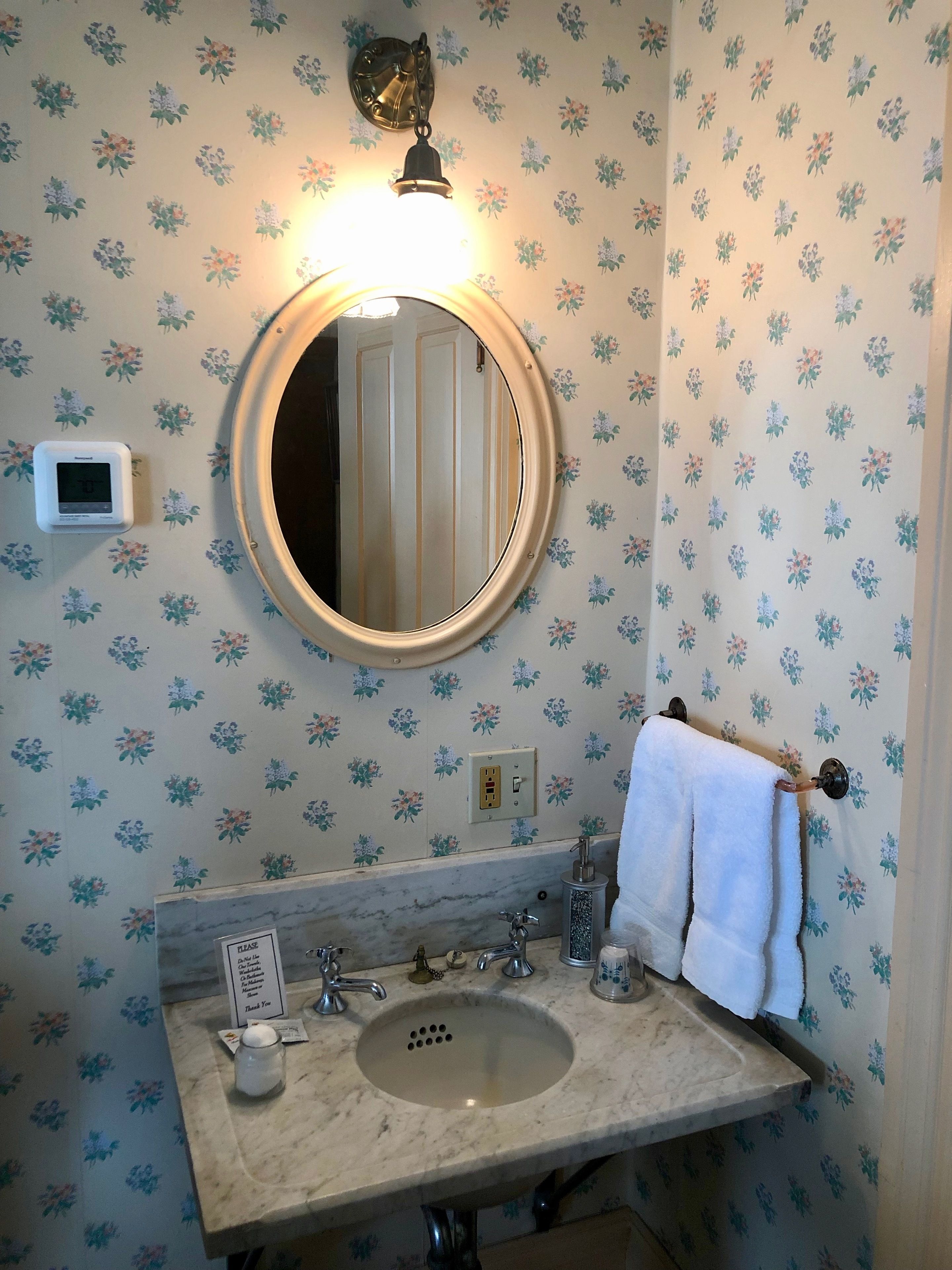 A bathroom with a round mirror, a sink, a towel rack, and a thermostat.