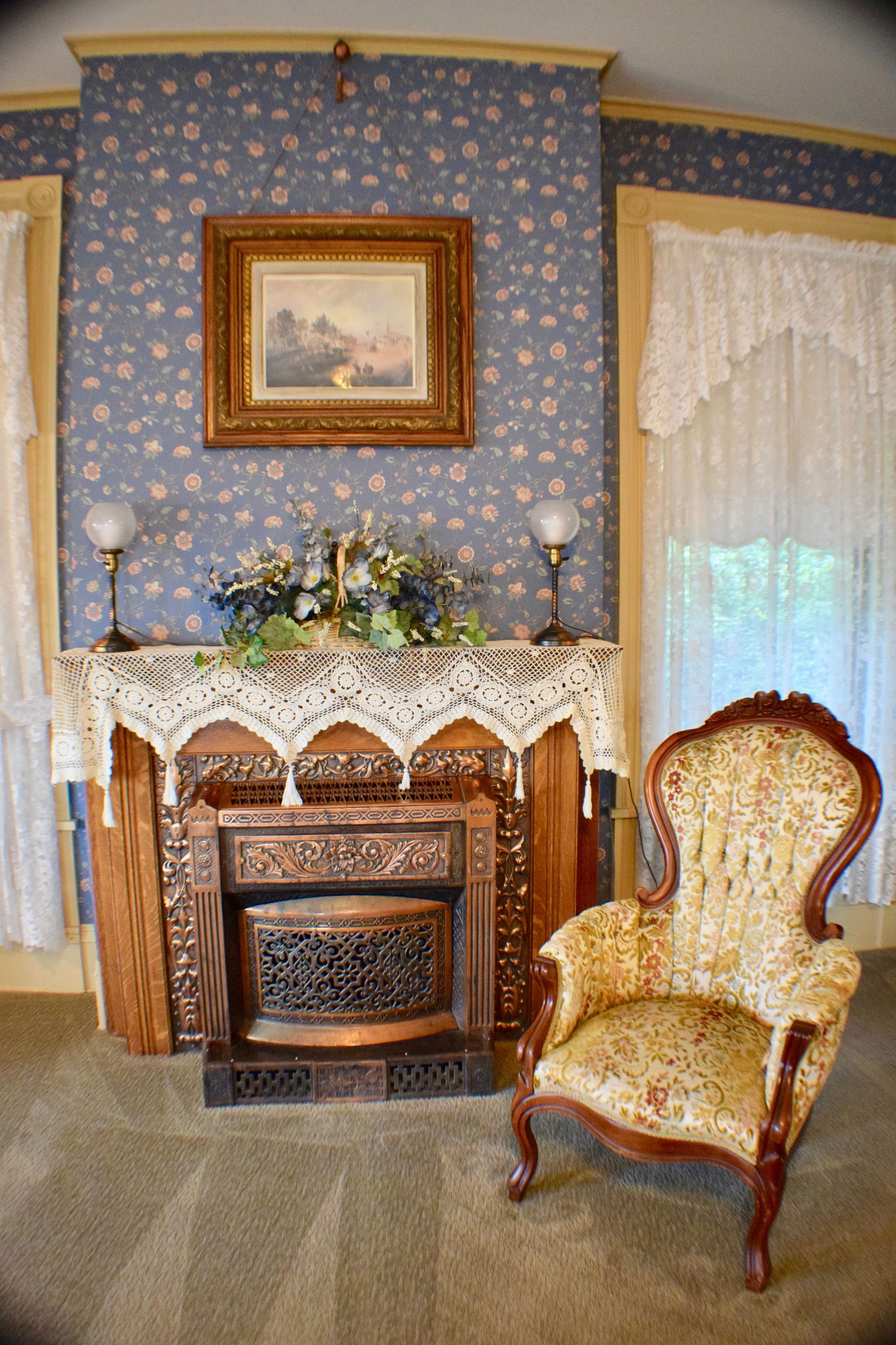 A room with a fireplace, a chair, and floral wallpaper.
