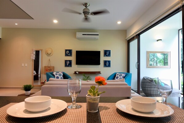 A modern hotel room with a large bed, a flat-screen TV, and a dining area with a table set for two.