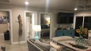 A modern living room with a sofa, coffee table, and a TV. There is a door leading to another room, and a blue lamp on the coffee table. - Paradise on the lake (Centre)