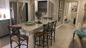 A modern kitchen with a stainless steel refrigerator, a dining area with bar stools, and a living room with a couch. - Paradise on the lake (Centre)