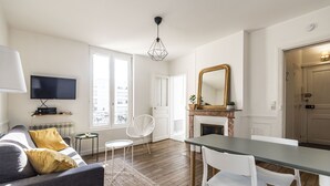 Una sala de estar moderna con sofá, mesa de comedor y sillas. Hay un televisor montado en la pared, una chimenea y un espejo grande.