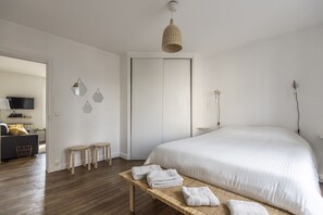 A bedroom with a large bed, a wooden bench with towels, a wardrobe, and a television in the adjacent room.