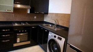 Une cuisine moderne avec des meubles de couleur noire, des appareils en acier inoxydable, un four encastré, un lave-linge et un réfrigérateur.