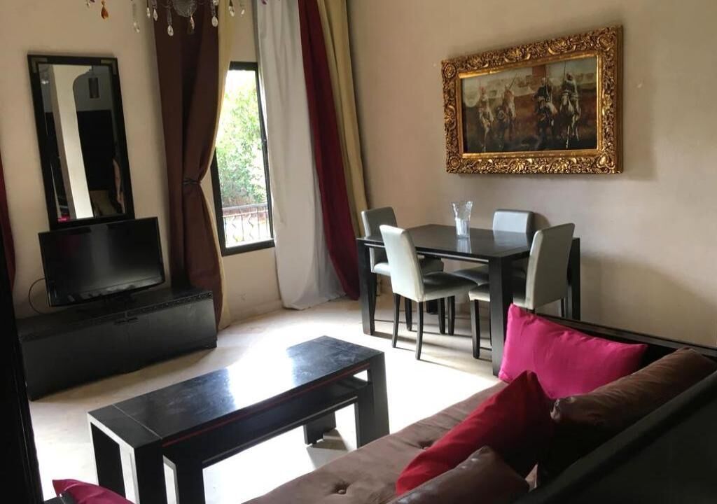 Una sala de estar con sofá, una mesa de centro, televisor, una mesa de comedor con sillas y un cuadro en la pared.