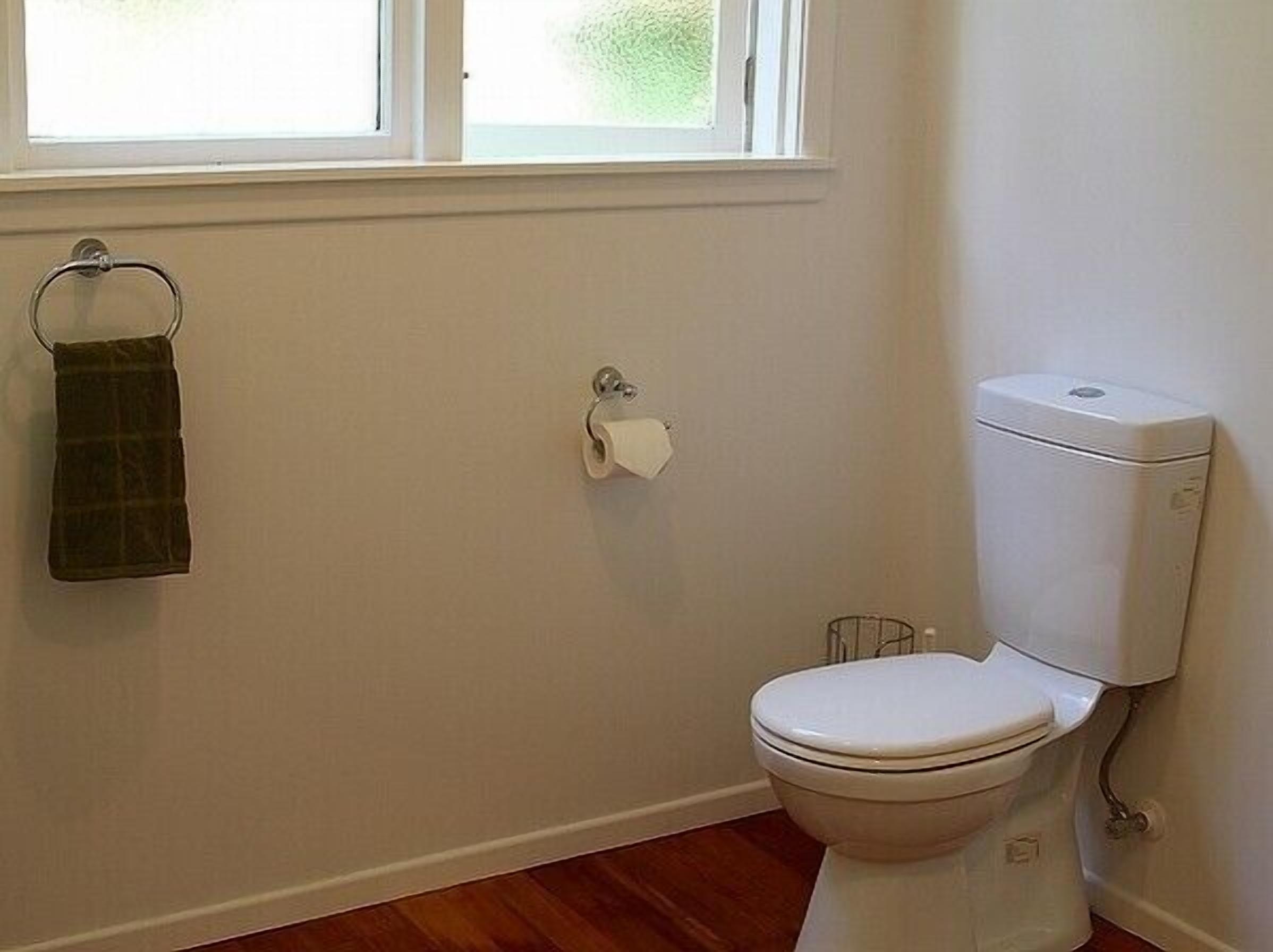 A small, clean bathroom with a toilet, a towel rack, and a window.