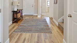 Un hall d’entrée spacieux, doté d’un parquet en bois, d’un tapis à motifs et de deux fenêtres en arc de cercle.