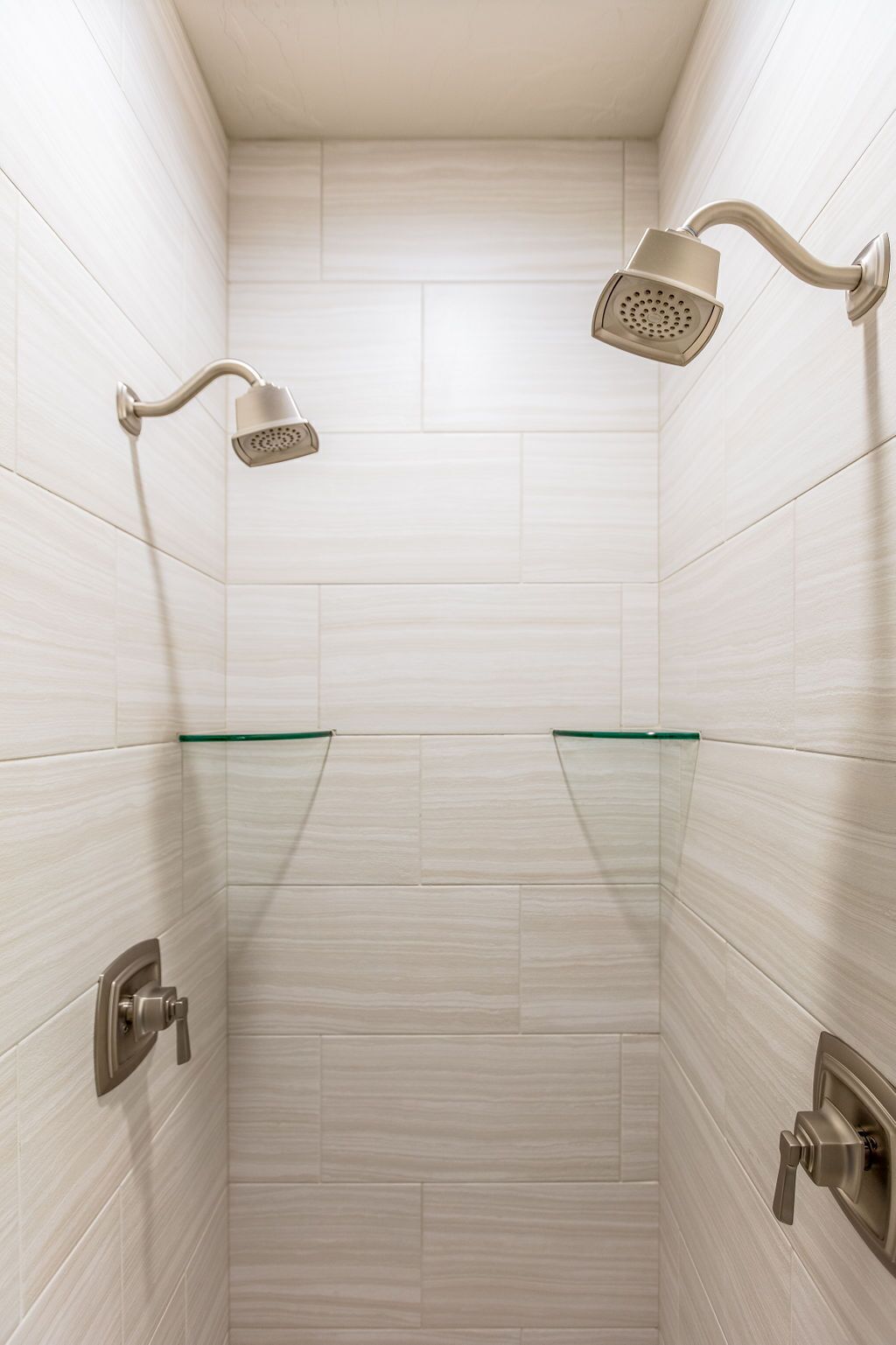 Ducha con dos cabezales de ducha de mano, estante de vidrio y grifo instalado en la pared.