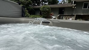 Un bain à remous dont l’eau éclabousse, entouré d’une maison avec un garage apparent et un arbre.
