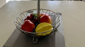 A dining table with a fruit basket containing green apples, red apples, and a yellow fruit.