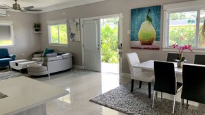 A modern living room with a white sofa, a blue armchair, a dining table with chairs, and a kitchen area.