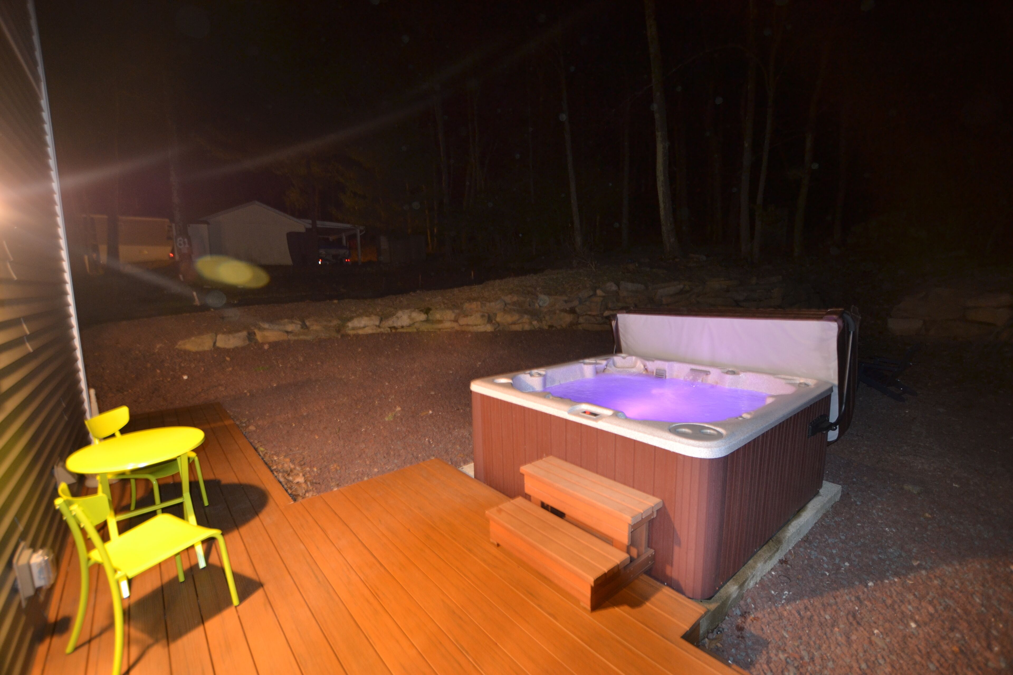 Un espace extérieur avec un jacuzzi, une terrasse en bois, un banc et une table avec des chaises.