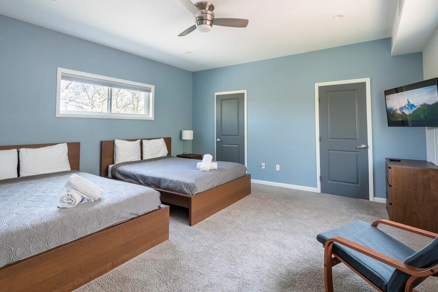 A bedroom with two beds, a ceiling fan, a TV, and a window.