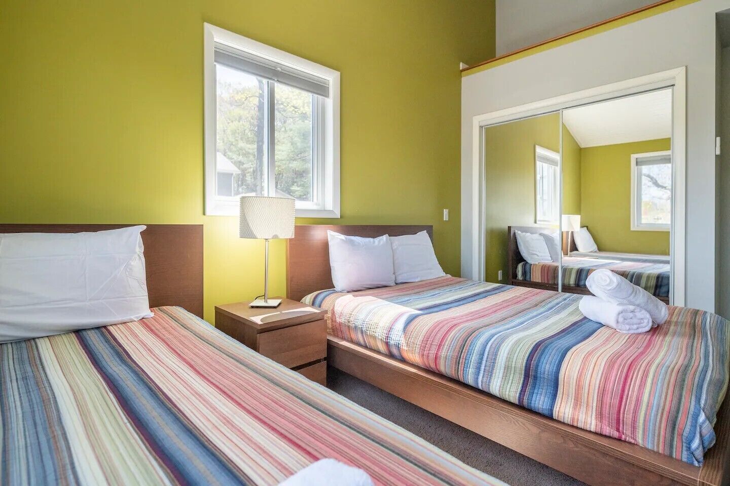 A hotel room with two beds, a window, a lamp, and a mirror.