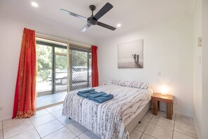 A bedroom with a bed, a ceiling fan, a window with curtains, and a bedside table with a lamp.