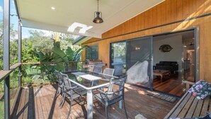 A modern outdoor deck with a glass table and chairs, wooden flooring, and a view of the surrounding greenery. - Theme parks paradise (Ormeau)