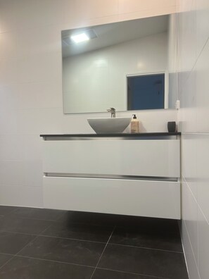 A modern bathroom with a white sink, a mirror, and a black tiled floor.