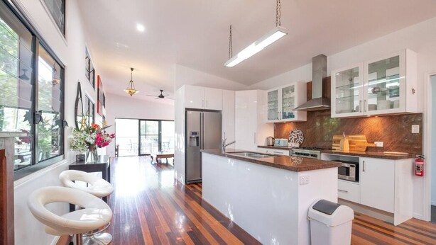 A modern kitchen with white cabinets, a central island, and a wooden floor. - Theme parks paradise (Ormeau)