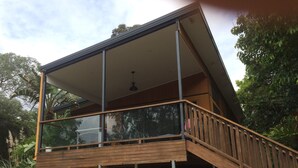 A modern house with a wooden deck and glass railings. - Theme parks paradise (Ormeau)