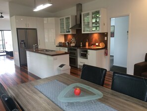 Une cuisine moderne avec des meubles blancs, des appareils en acier inoxydable et un coin repas comprenant une table et des chaises en bois.