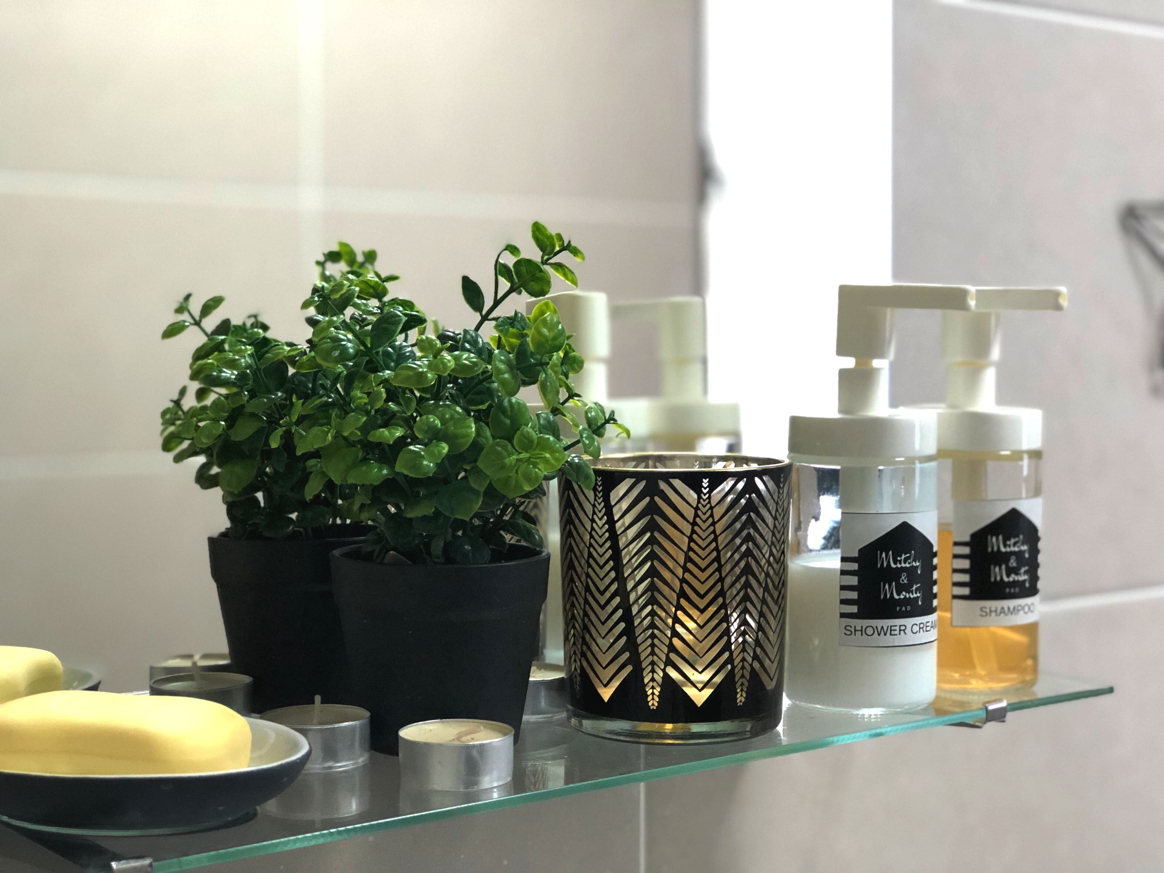Een badkamerschaar met een bloempot, een decoratieve kaars en twee flessen shampoo en douchecrème.