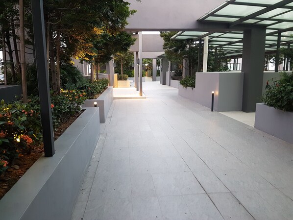 Un paseo techado con suelo de baldosas, rodeado de macetas con plantas y flores.