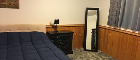A bedroom with a bed, a dresser, a mirror, and a window with curtains.