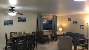 A living room with a dining table, chairs, a sofa, and a rocking chair. There are two ceiling fans, a window with curtains, and framed pictures on the walls. - Sage House- in town with LOTS of space (Ennis)