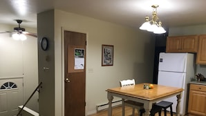 A kitchen with wooden cabinets, a white refrigerator, a wooden dining table with two stools, a ceiling fan, and a wall-mounted clock. - Sage House- in town with LOTS of space (Ennis)