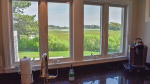 A kitchen with a large window overlooking a green landscape.