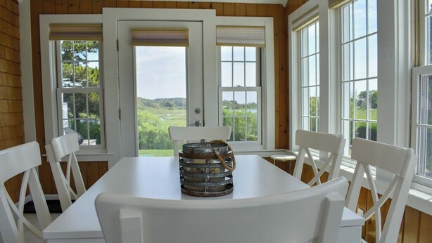 A dining area with a white table and chairs, a metal lantern, and large windows with a view of greenery.