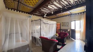 A room with a bed under a canopy, a wicker chair, and a small table with a vase.
