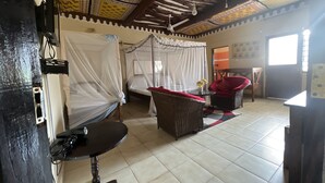 A room with a bed, a chair, a small table, a ceiling fan, and a window.