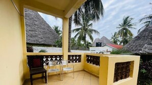 A covered balcony with tiled flooring, a wooden bench, and two metal chairs.