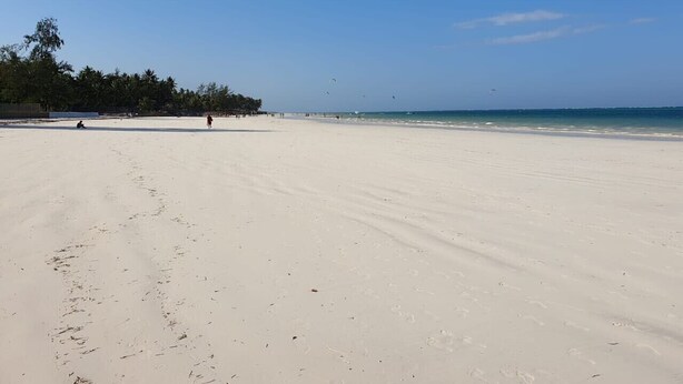 A wide sandy beach with a clear blue sky and calm sea.