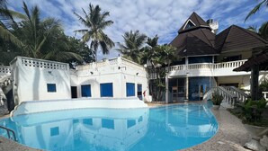 A swimming pool with a tiled deck, surrounded by a building with a balcony and a staircase.