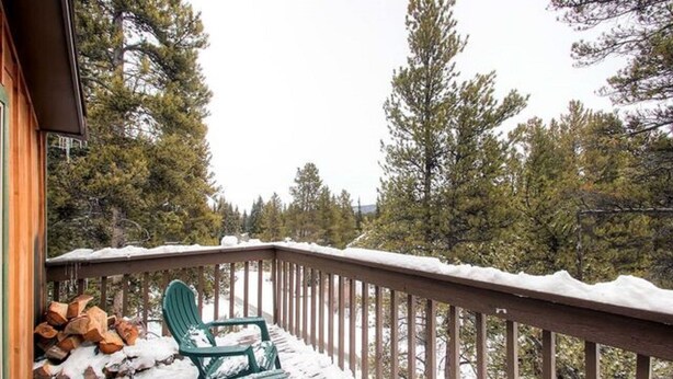 Une terrasse en bois avec un fauteuil Adirondack vert et une rambarde recouverte de neige.