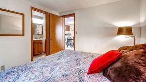 Une chambre à coucher comprenant un lit, une table de chevet, une lampe et une porte donnant sur une salle de bain.