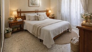 Un dormitorio con cama, mesitas de noche, una lámpara, un cuadro enmarcado, una ventana con cortinas y una cesta en el suelo.